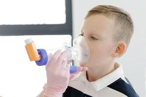 Boy with allergic asthma, inhaling his medication through spacer while sitting in doctors office photo