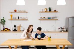 A young woman helps a boy with his lessons using a tablet and a globe. A homeschooling student does his homework with the help of a tutor photo