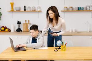 A young woman helps a boy with his lessons using a tablet and a globe. A homeschooling student does his homework with the help of a tutor photo