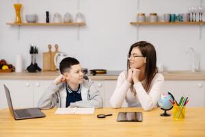 A young woman helps a boy with his lessons using a tablet and a globe. A homeschooling student does his homework with the help of a tutor photo