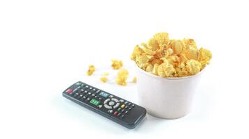 Isolated image of popcorn in paper cup and TV remote control set against a white background, showcasing the fluffy, perfect for themes related to snacks, cinema, or casual dining. photo