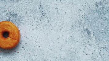 Pink glazed donut falling on gray cement background. Top view of fall doughnut video
