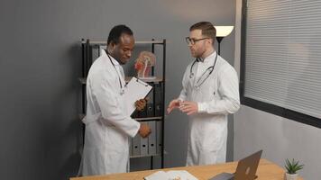 Happy hospital colleagues men shaking hands in office, talking, discussing teamwork video