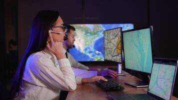 Young Female Technical Support Specialist to a Handsome Colleague Talking on a Headset while Working on a Computer in Transport Control Room Filled with Displays video