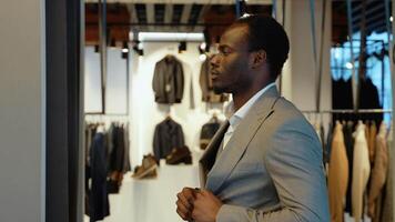 Young man choosing and trying jacket or suit and looking to mirror in dressing room video