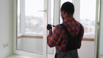 Workman in overalls installing or adjusting plastic windows in the living room at home video