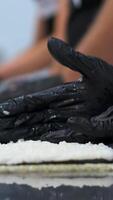 Hands of a professional sushi chef laying out rice on Nori leaves lying on a bamboo mat on a white kitchen table with a row of fresh vegetables, bell peppers and lettuce leaves laid out. video