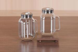 Transparent glass mug jar with stainless steel metal lid and handle placed on a wooden table. Suitable for branding your product with quality 3d rendering. Empty drinking glass, realistic mock-up photo