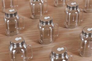 Transparent glass mug jar with stainless steel metal lid and handle placed on a wooden table. Suitable for branding your product with quality 3d rendering. Empty drinking glass, realistic mock-up photo