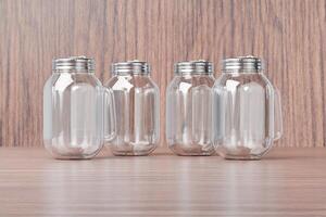 Transparent glass mug jar with stainless steel metal lid and handle placed on a wooden table. Suitable for branding your product with quality 3d rendering. Empty drinking glass, realistic mock-up photo