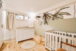 A baby's room with a crib, a dresser and a wall with a palm tree photo