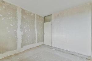 A room with a white door and a wall covered in drywall photo