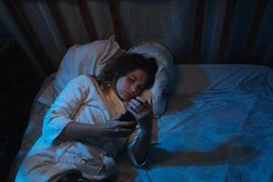 Insomnia. Person cannot fall asleep, using smartphone lying in bed at night. photo