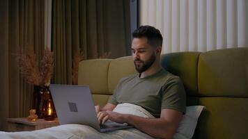 Caucasian man bed remote working laptop typing home computer gadget businessman entrepreneur employee male freelancer desk internet programmer browsing user networking technology business bedroom guy video