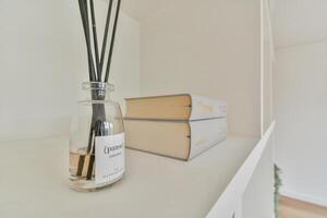 A white shelf with a book and a bottle of reed photo