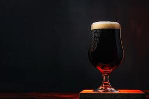 A glass of dark beer sitting on a wooden block photo