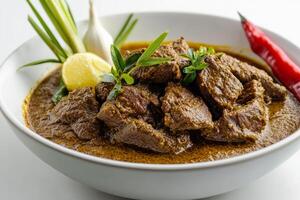 A bowl of beef curry with a lemon wedge and a red chili photo