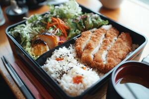 A bento box with rice, chicken, vegetables and a cup of tea photo