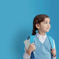 A little girl in a school uniform holding a book and a backpack photo