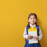 Asian little girl holding a notebook and standing against a yellow background photo