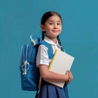 A little girl in a school uniform holding a book and a backpack photo