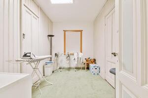 A laundry room with a washing machine, ironing board and a teddy bear photo