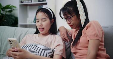 Footage handheld shot, Asian mother and young woman are looking at a smartphone together on sofa. They sit closely, sharing a quiet moment as they enjoy something on the screen video