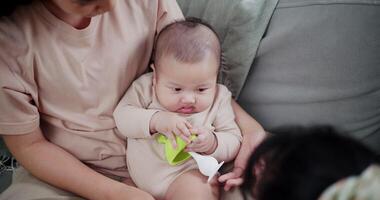 Handheld high angle view shot, Mother and daughter are having fun playing with little boy on the sofa in the cozy living room at home. Loving and warm family video