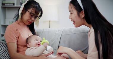 Handheld shot, Mother and daughter are having fun playing with little boy on the sofa in the cozy living room at home. Loving and warm family video