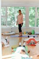 A skilled trainer oversees a group of senior women practicing various yoga exercises, including neck, back, and leg stretches, in a sunlit space, promoting wellness and harmony photo