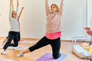A group of senior women engage in various yoga exercises, including neck, back, and leg stretches, under the guidance of a trainer in a sunlit space, promoting well-being and harmony photo