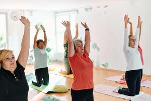 A group of senior women engage in various yoga exercises, including neck, back, and leg stretches, under the guidance of a trainer in a sunlit space, promoting well-being and harmony photo