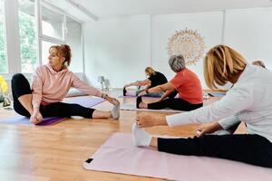 A group of senior women engage in various yoga exercises, including neck, back, and leg stretches, under the guidance of a trainer in a sunlit space, promoting well-being and harmony photo