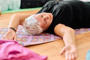 In a sunlit space, a senior woman gracefully practices rejuvenating yoga, focusing on neck, back, and leg stretches, embodying serenity and well-being photo