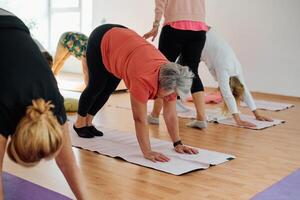 A group of senior women engage in various yoga exercises, including neck, back, and leg stretches, under the guidance of a trainer in a sunlit space, promoting well-being and harmony photo