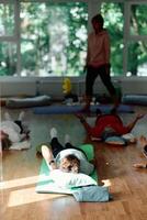 A group of senior women engage in various yoga exercises, including neck, back, and leg stretches, under the guidance of a trainer in a sunlit space, promoting well-being and harmony photo