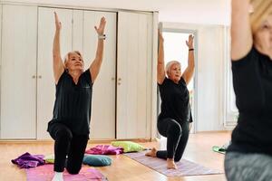 A group of senior women engage in various yoga exercises, including neck, back, and leg stretches, under the guidance of a trainer in a sunlit space, promoting well-being and harmony photo