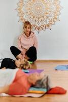 A skilled trainer oversees a group of senior women practicing various yoga exercises, including neck, back, and leg stretches, in a sunlit space, promoting wellness and harmony photo
