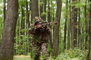 A highly skilled elite sniper, camouflaged in the dense forest, stealthily maneuvers through dangerous woodland terrain on a covert and precise mission photo