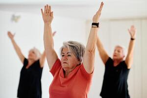 A group of senior women engage in various yoga exercises, including neck, back, and leg stretches, under the guidance of a trainer in a sunlit space, promoting well-being and harmony photo
