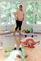 A skilled trainer oversees a group of senior women practicing various yoga exercises, including neck, back, and leg stretches, in a sunlit space, promoting wellness and harmony photo