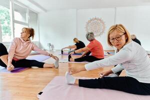 A group of senior women engage in various yoga exercises, including neck, back, and leg stretches, under the guidance of a trainer in a sunlit space, promoting well-being and harmony photo