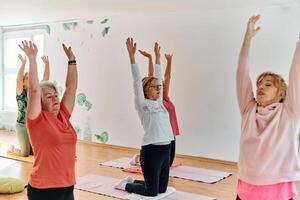 A group of senior women engage in various yoga exercises, including neck, back, and leg stretches, under the guidance of a trainer in a sunlit space, promoting well-being and harmony photo