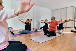 A group of senior women engage in various yoga exercises, including neck, back, and leg stretches, under the guidance of a trainer in a sunlit space, promoting well-being and harmony photo