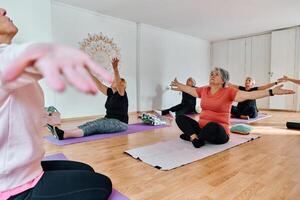 A group of senior women engage in various yoga exercises, including neck, back, and leg stretches, under the guidance of a trainer in a sunlit space, promoting well-being and harmony photo
