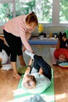 A skilled trainer oversees a group of senior women practicing various yoga exercises, including neck, back, and leg stretches, in a sunlit space, promoting wellness and harmony photo