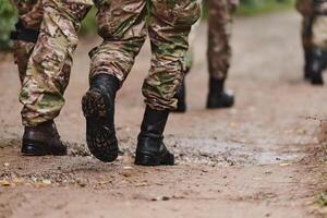 Close up photo, the resilient legs of elite soldiers, clad in camouflage boots, stride purposefully along a hazardous forest path as they embark on a high-stakes military mission photo