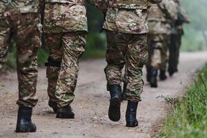 Close up photo, the resilient legs of elite soldiers, clad in camouflage boots, stride purposefully along a hazardous forest path as they embark on a high-stakes military mission photo