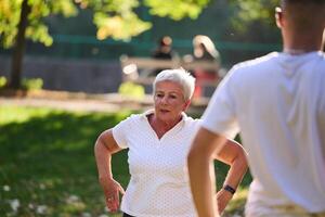 A group of seniors follows a trainer, engaging in outdoor exercises in the park, as they collectively strive to maintain vitality and well-being, embracing an active and health-conscious lifestyle in photo