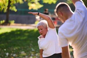 A group of seniors follows a trainer, engaging in outdoor exercises in the park, as they collectively strive to maintain vitality and well-being, embracing an active and health-conscious lifestyle in photo